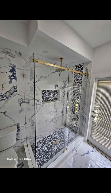 Walk-in shower remodel with marble-look tile, pebble mosaic, and brushed gold hardware