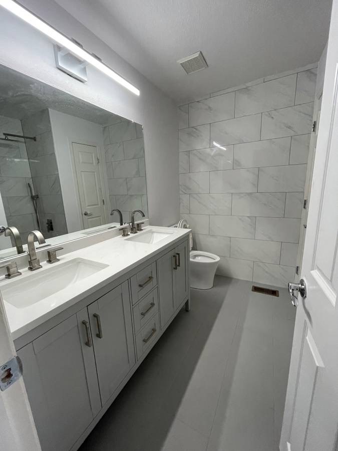 Modern bathroom remodel with a gray double vanity, marble-look tile, and LED mirror light